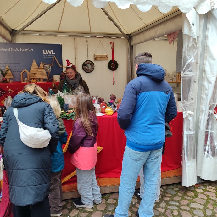 Eine Familie in dicken Jacken steht draußen vor einem Verkaufsstand auf dem Weihnachtsmarkt. (vergrößerte Bildansicht wird geöffnet)