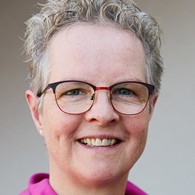 lächelnde Frau mit kurzen blonden Locken und Brille
