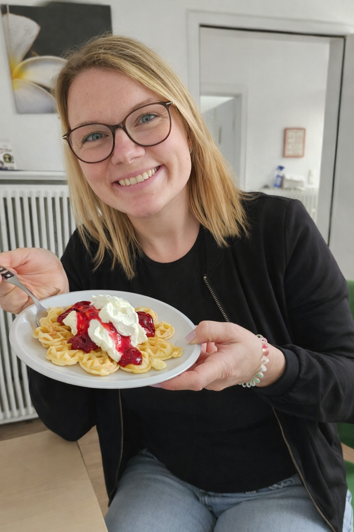 eine blonde Frau isst eine Waffeln mit Eis, Sahne und heißen Kirschen